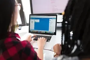 a woman is typing on a laptop computer while another woman looks on .