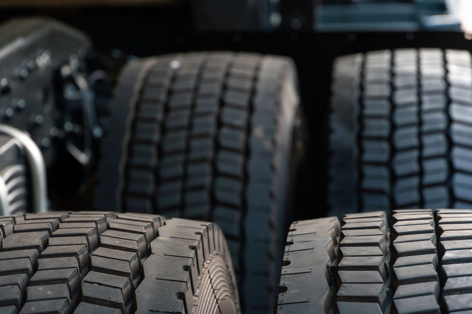 Close-up of large black truck tires stacked in a row, with a vehicle visible in the background.