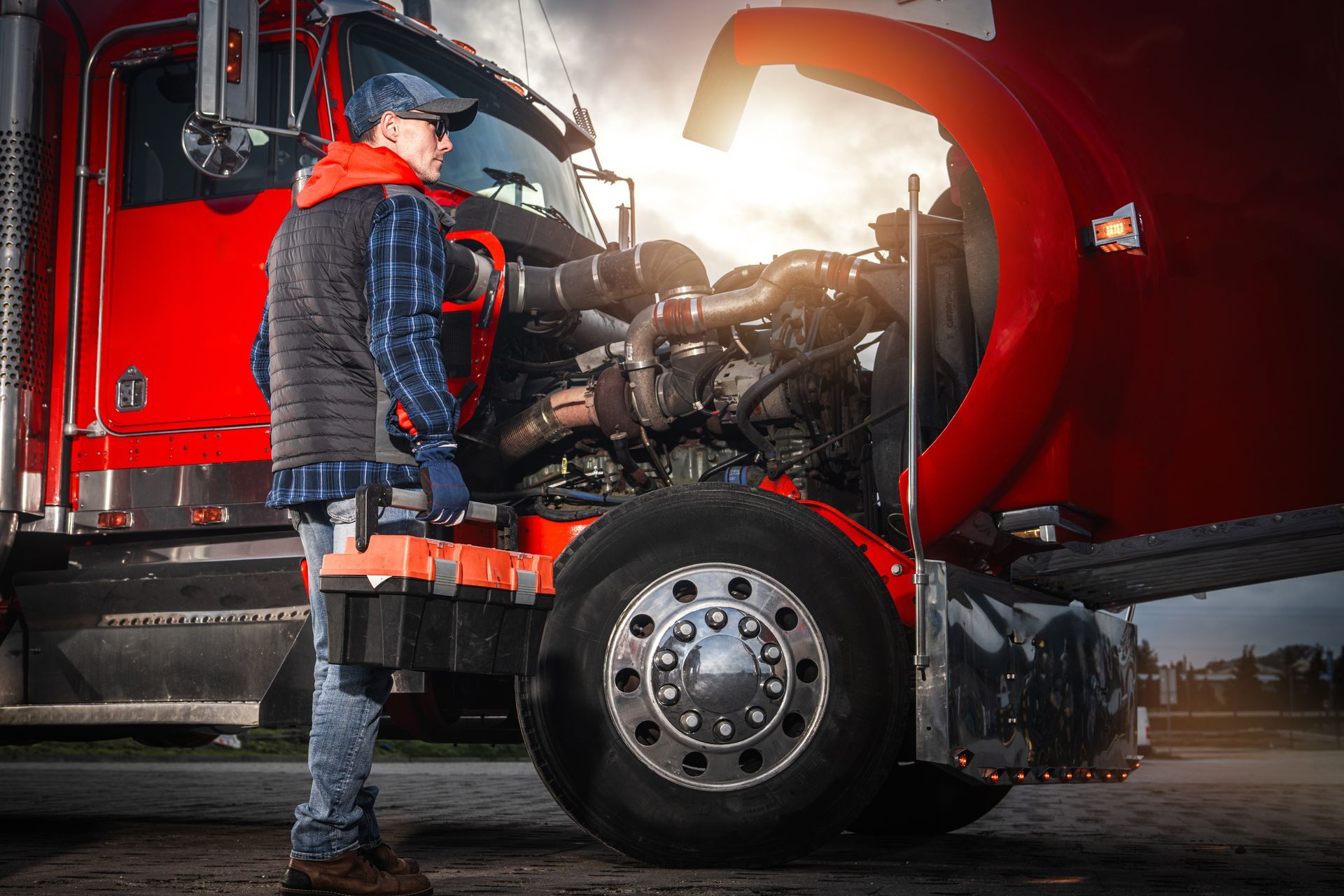 Truck driver inspecting engine of a red semi-truck at sunset