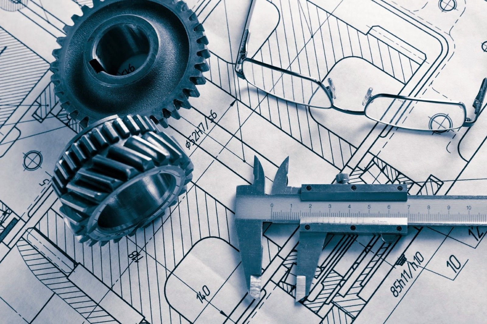Gears and calipers on top of an engineering blueprint, with glasses.