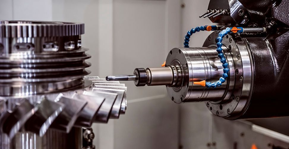 CNC machine milling a metal gear. Close-up with coolant hoses visible.