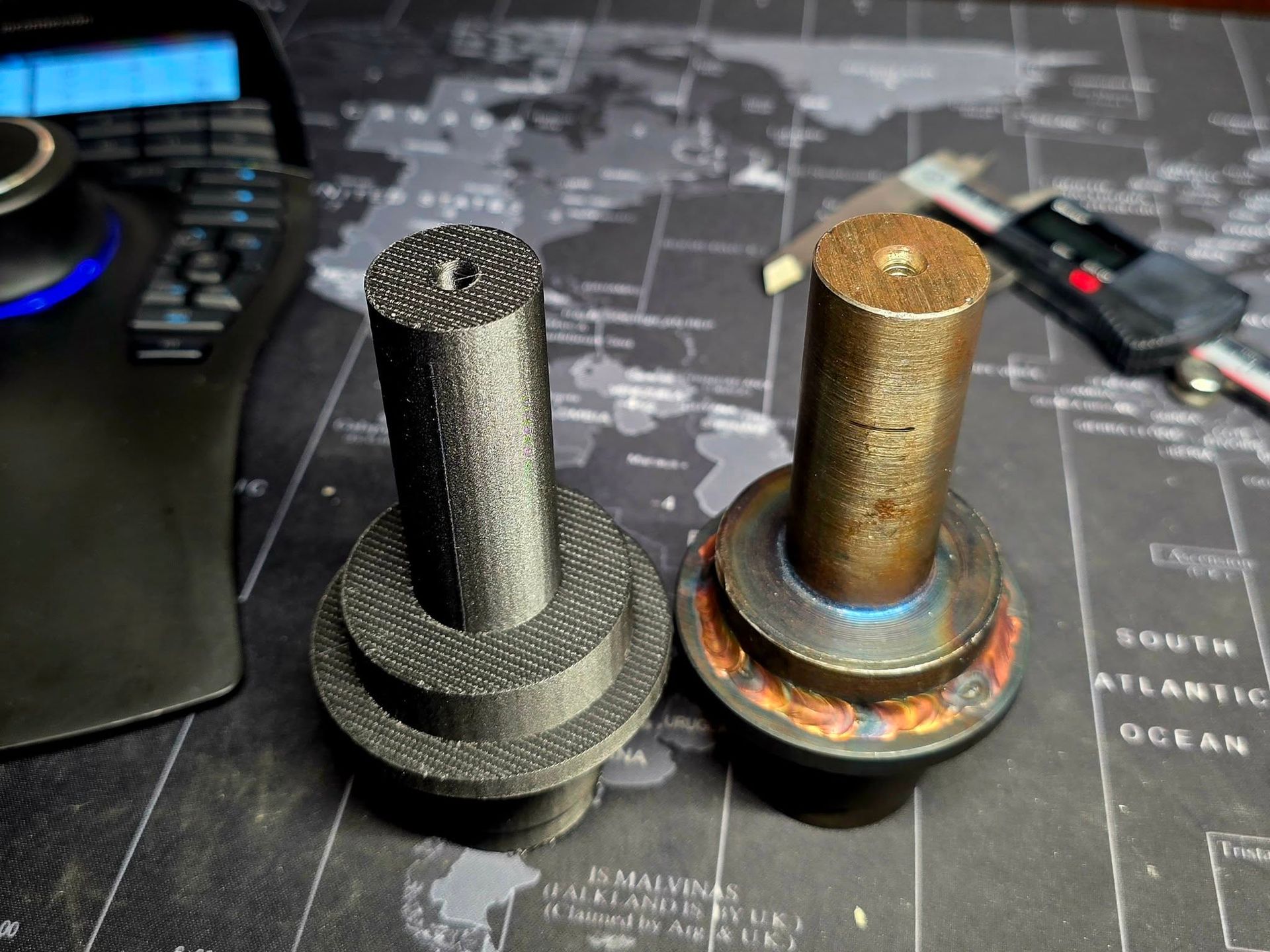 Two cylindrical parts; one black, 3D printed, the other brown, possibly metal, next to a digital caliper.