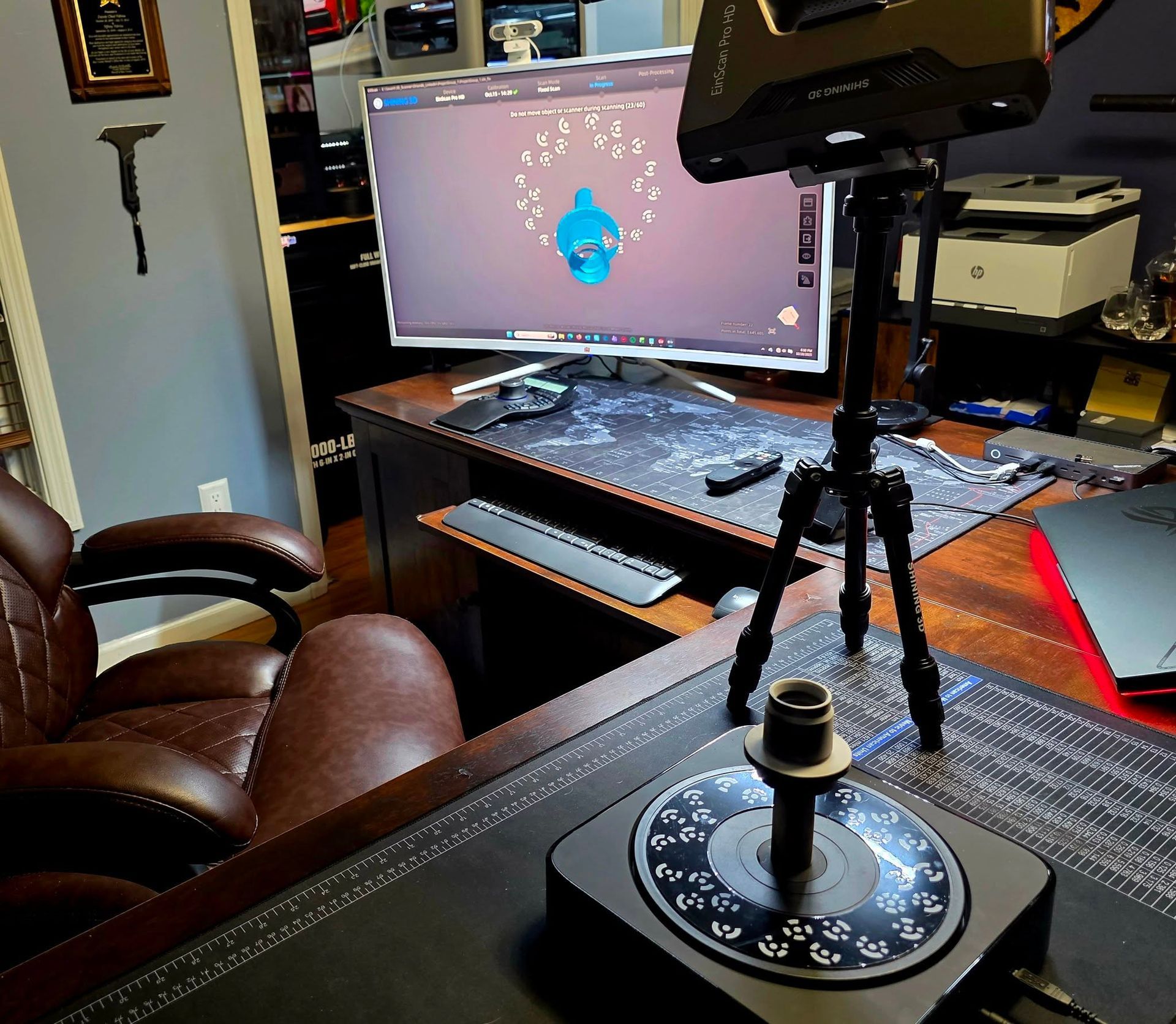 A 3D scanning setup with a monitor displaying a blue object, a tripod-mounted scanner, and a rotating base.