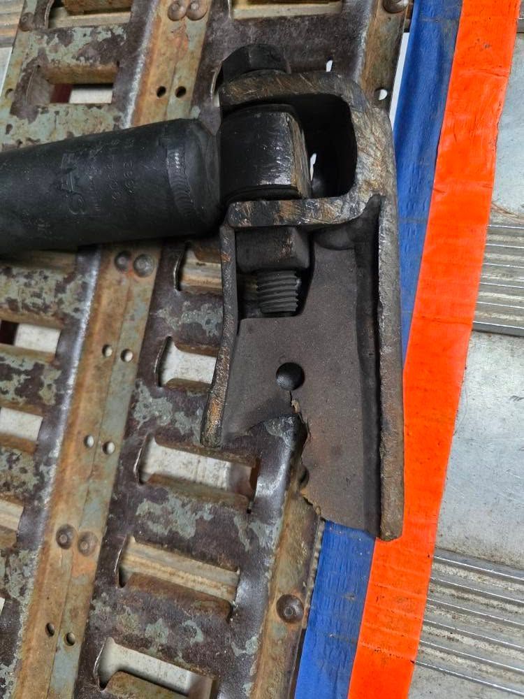 A close-up of a metal coupling attached to a track, with a bolt and nut. Blue and orange straps are visible.