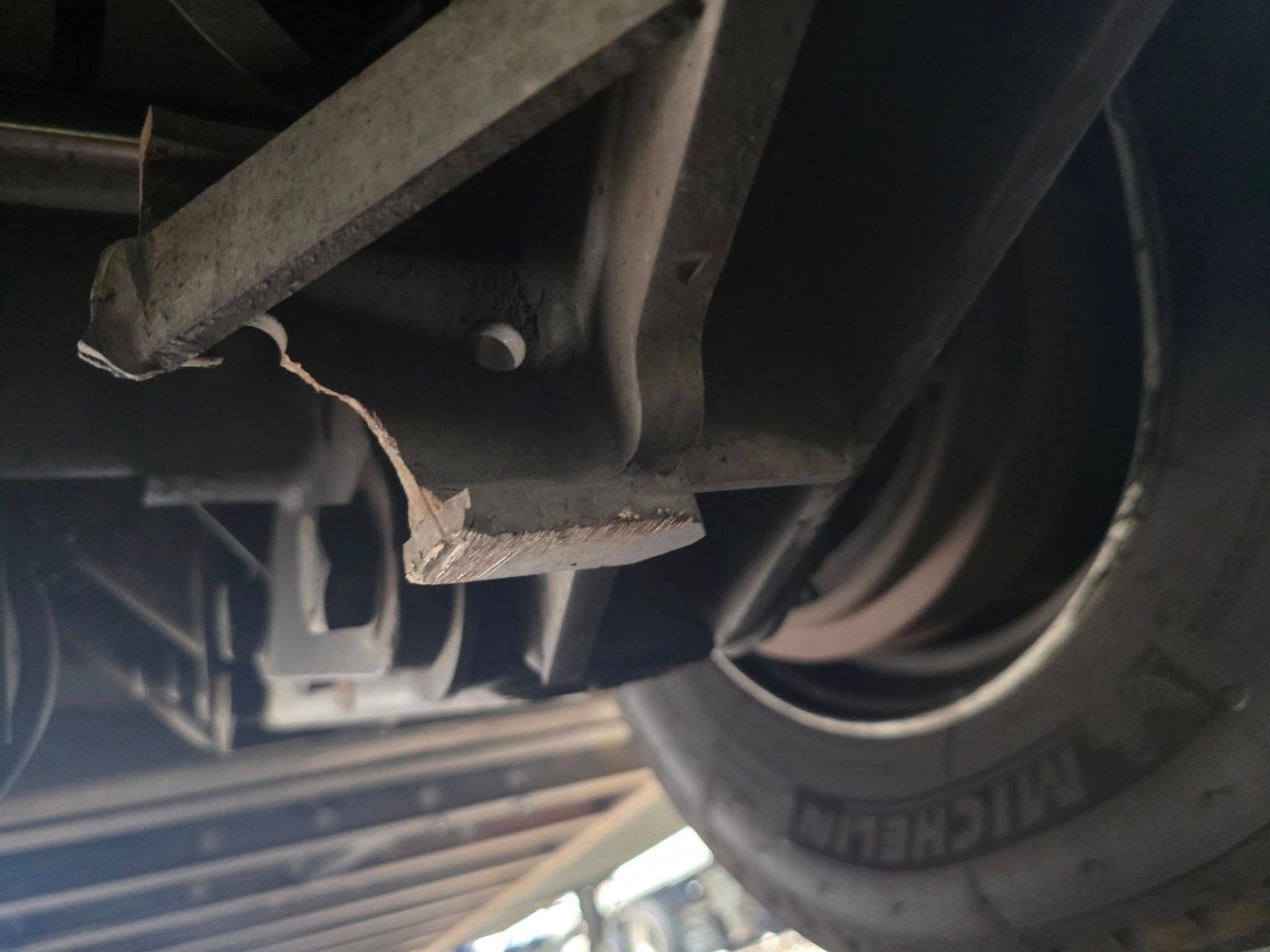 Damaged car suspension component with torn metal, viewed from below near tire.