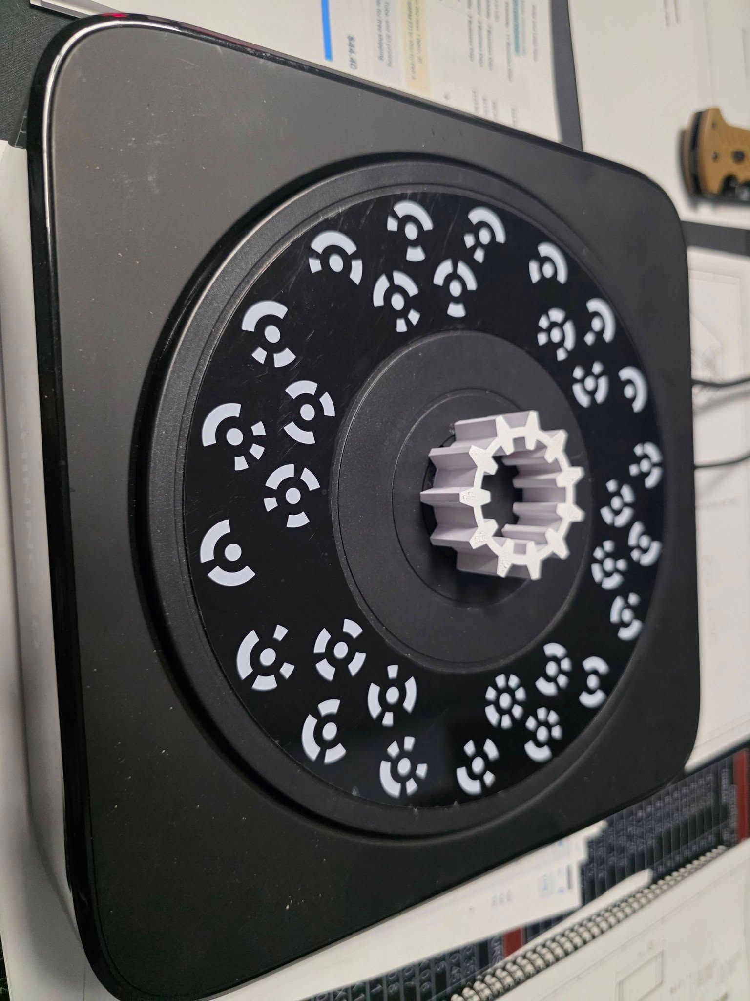 Black turntable with a 3D-printed gear centered on it, surrounded by white patterned lights.