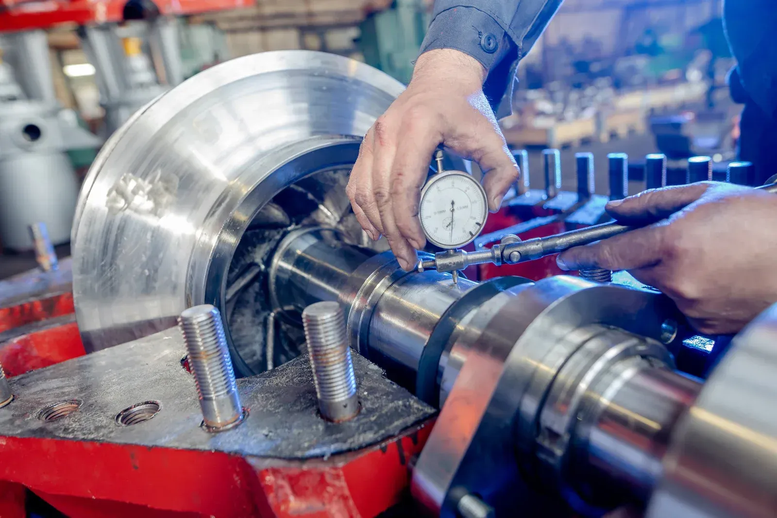 A person uses a dial indicator to precisely measure a metal industrial part on a factory machine.