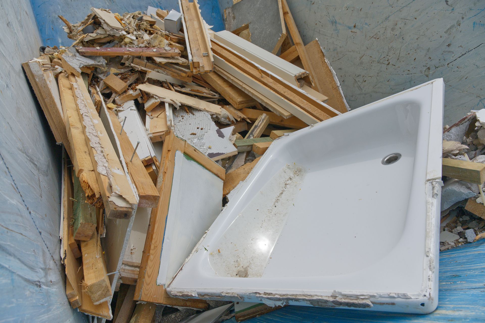 A demolition dumpster filled with construction debris, including a white shower pan and wooden planks.