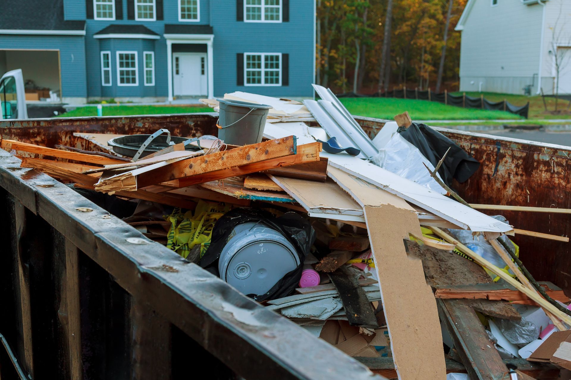 Construction debris overflowing a dumpster in front of a blue house.
