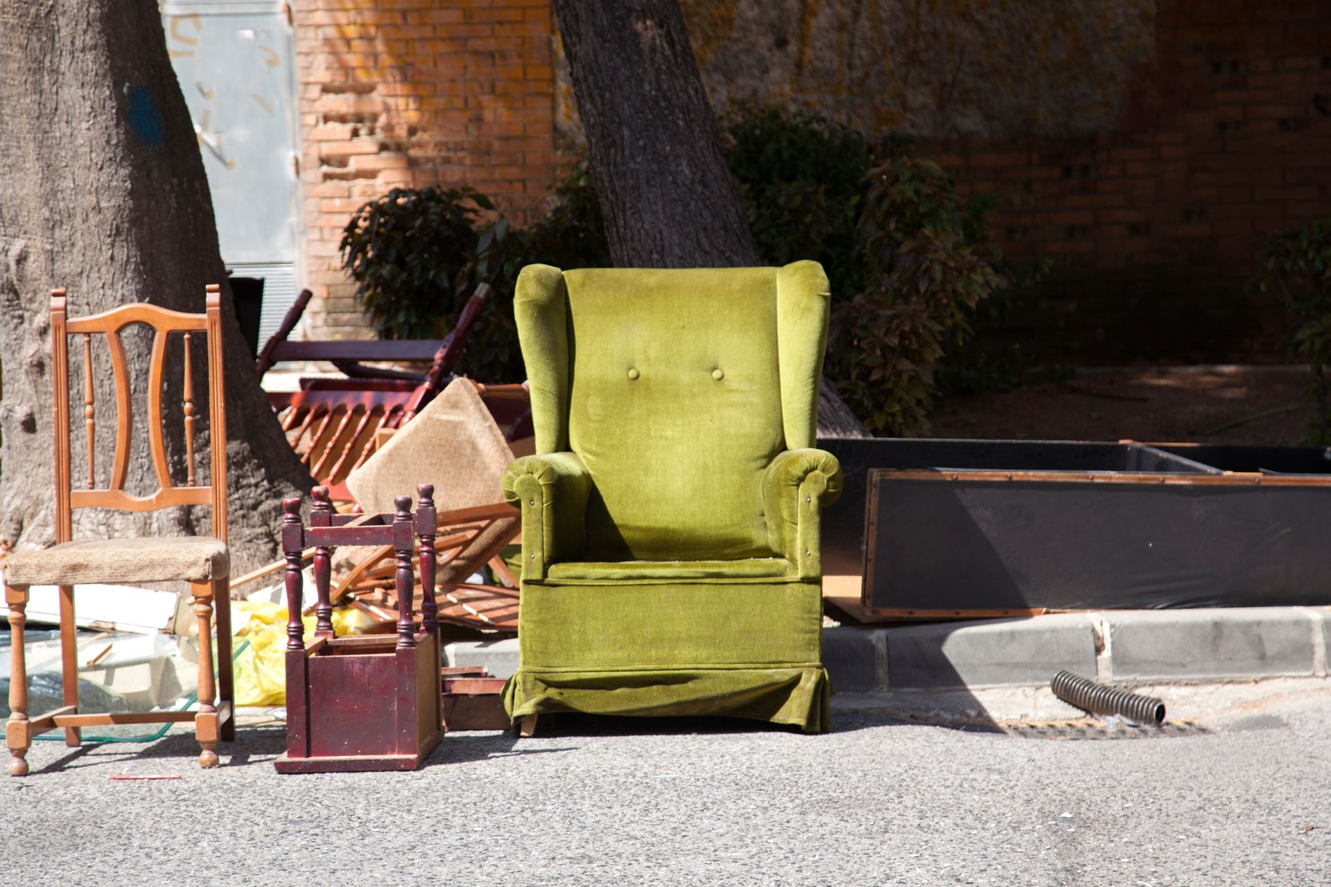 Discarded furniture, including a green armchair, and wooden chairs on a city sidewalk.