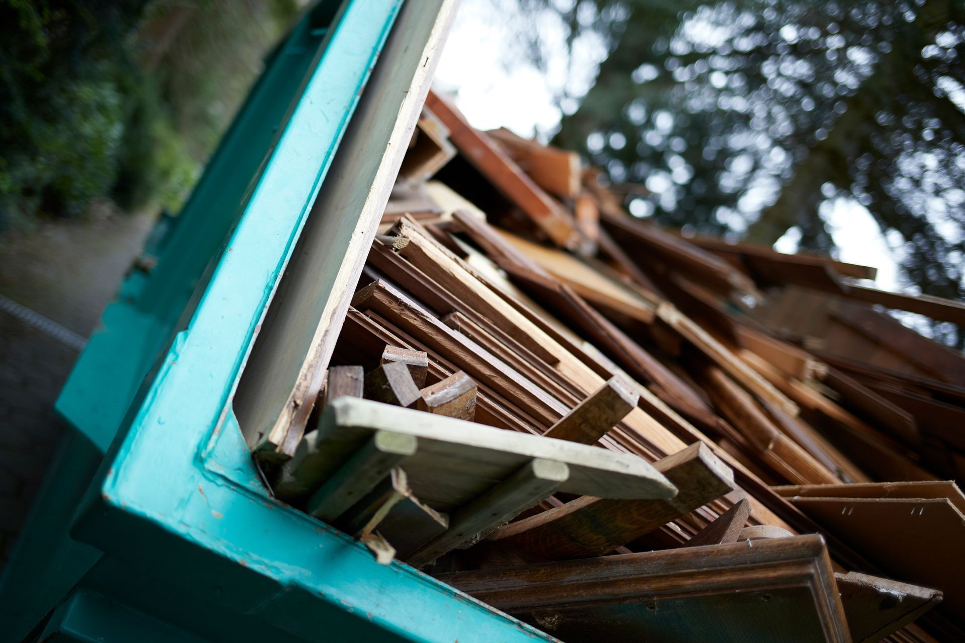 Green dumpster overflowing with wood scraps, viewed from a low angle.