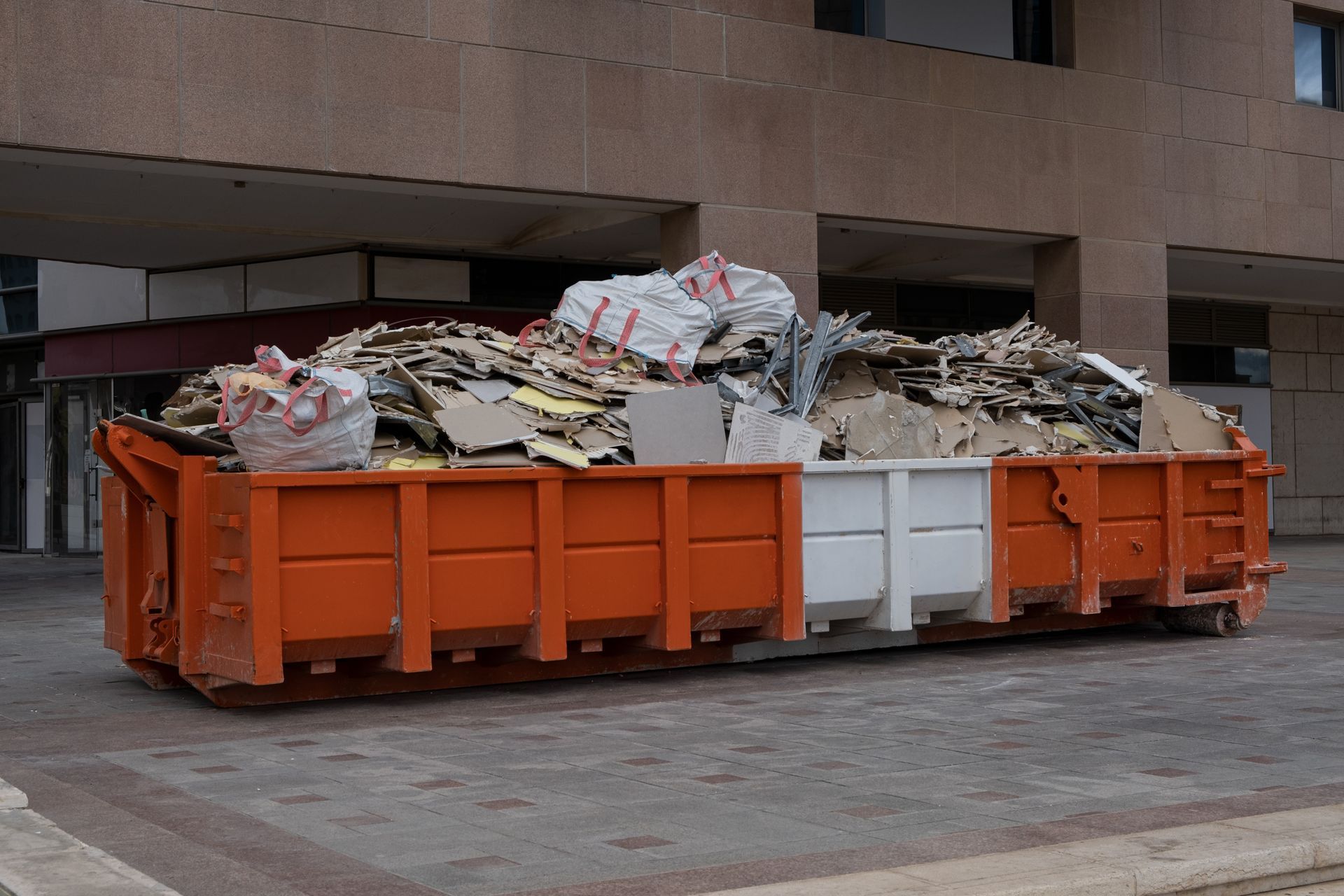 Orange and white dumpster overflowing with construction debris in front of a building.