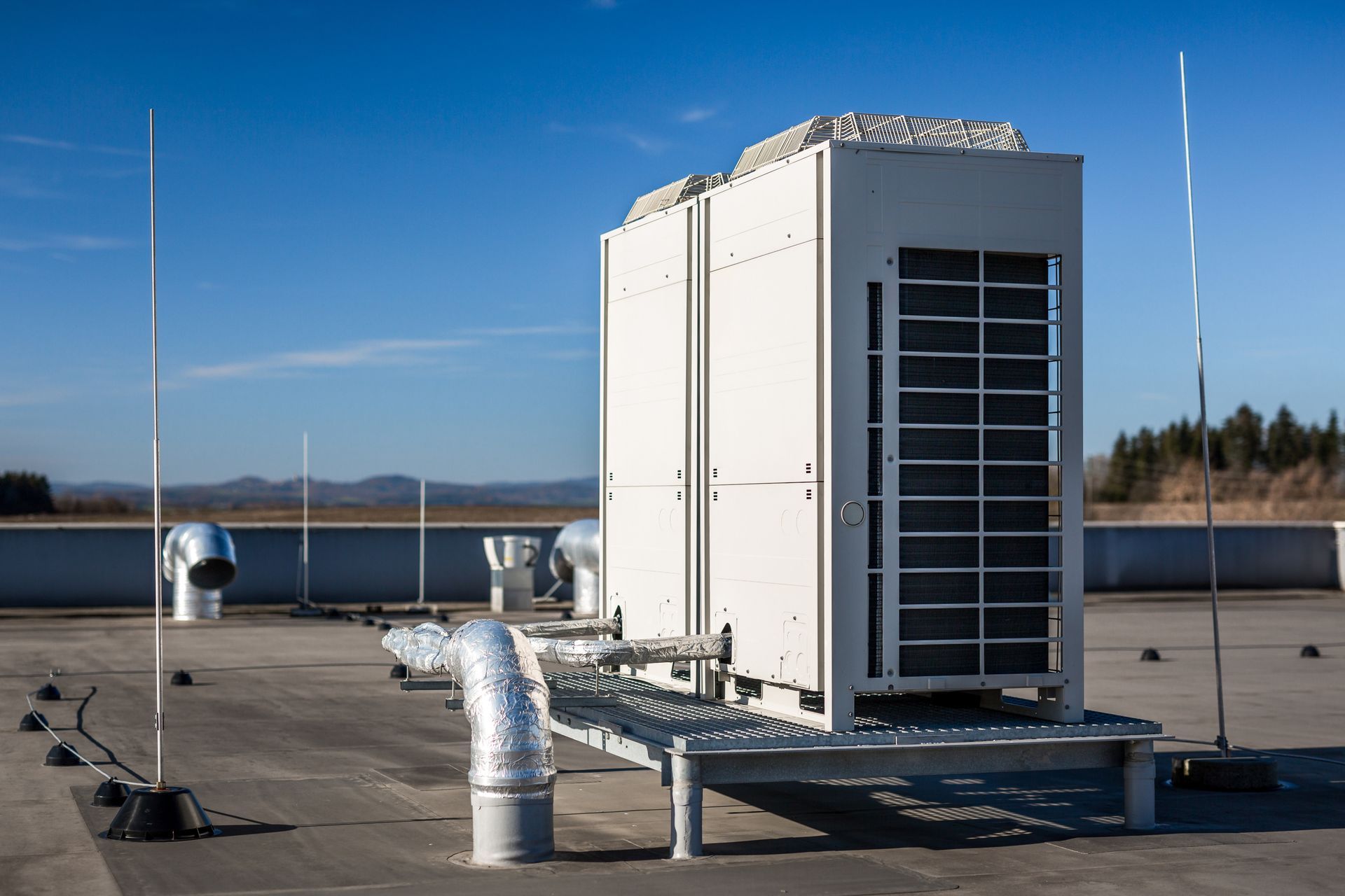 Rooftop HVAC unit beside a lake, with metallic ducts and antennas under a clear blue sky Rooftop HVAC unit beside a lake, with metallic ducts and antennas under a clear blue sky