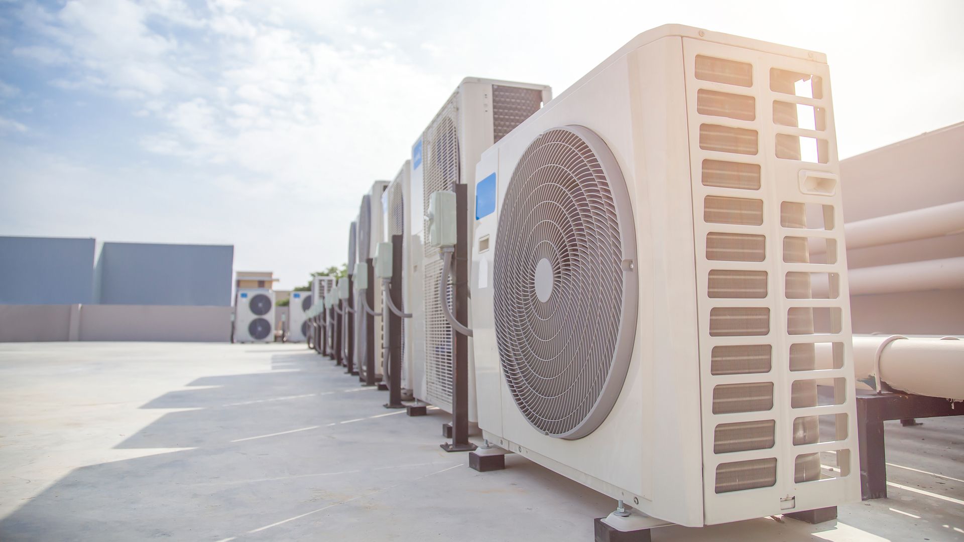 Row of rooftop air-conditioning units with large circular fans in bright sunlight Row of rooftop air-conditioning units with large circular fans in bright sunlight