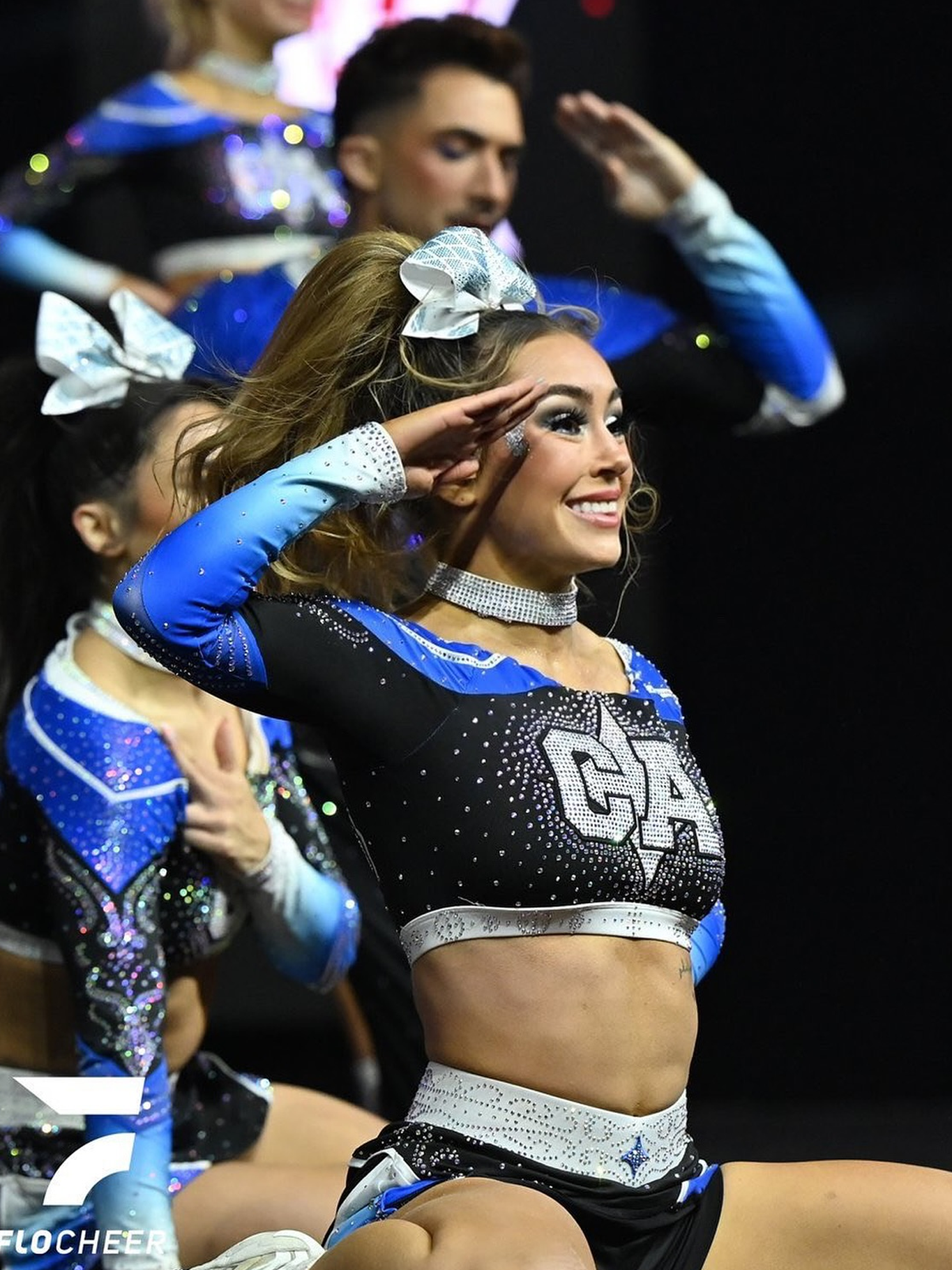 Cheerleader in blue and black uniform salutes, smiling during a performance.
