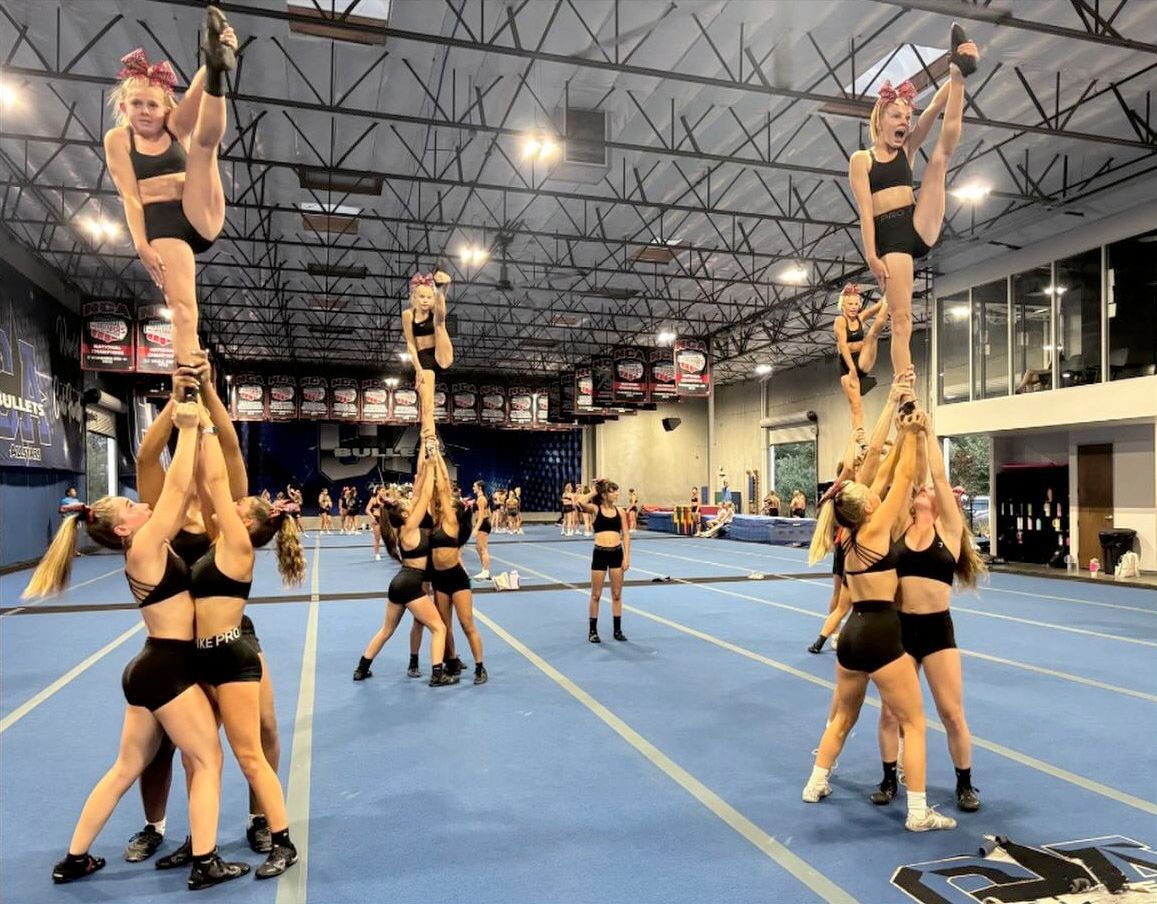 Cheerleaders in black uniforms performing high stunts in a gym.