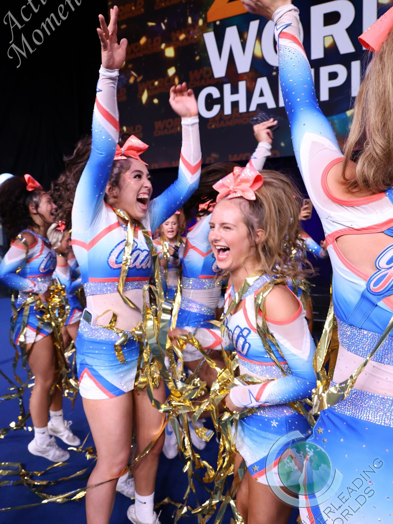 Cheerleaders in blue uniforms celebrating with arms raised after winning a world championship; gold confetti.