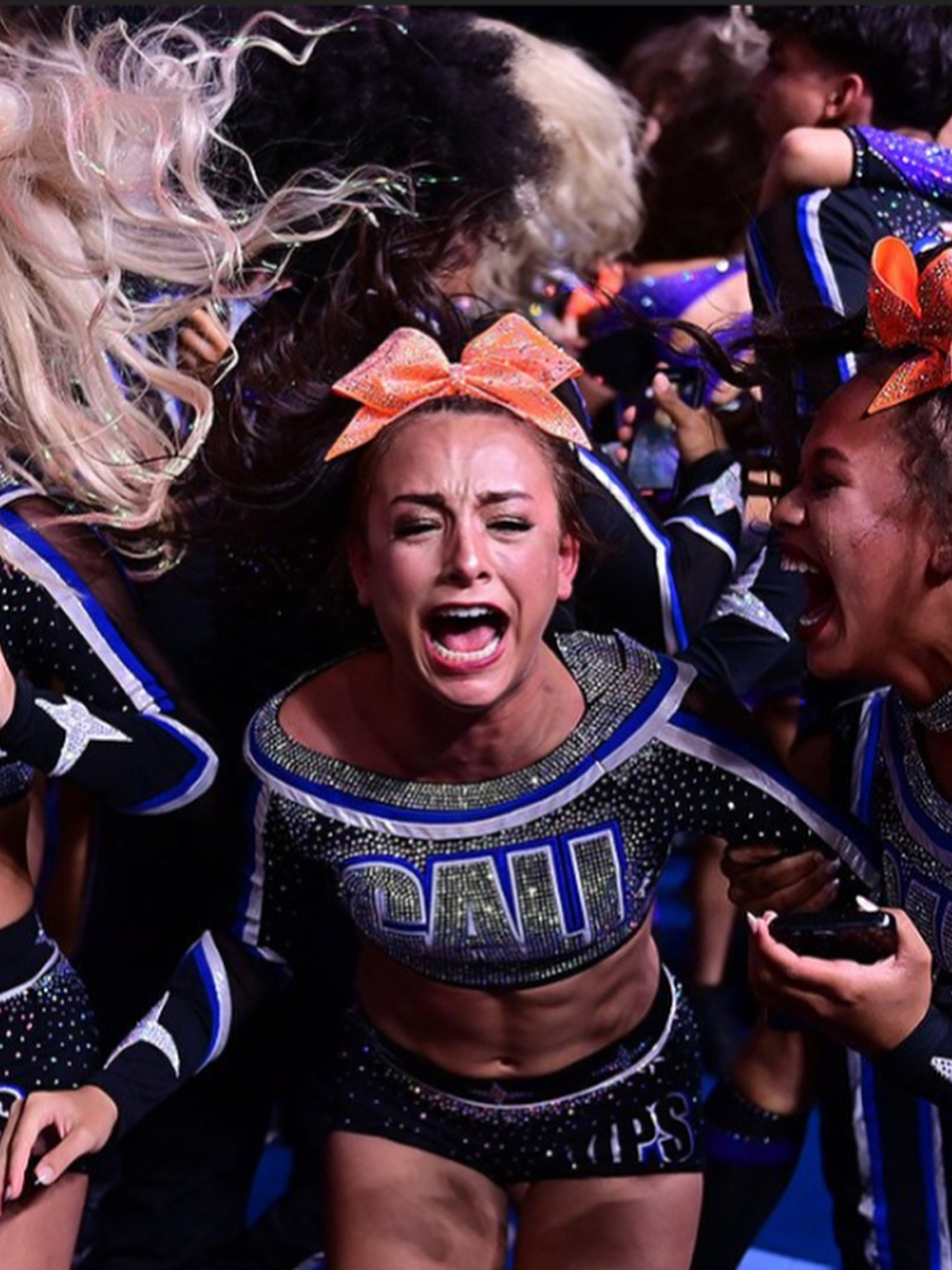 Cheerleaders in black and silver uniforms celebrating; one woman cries out in joy, orange bow.