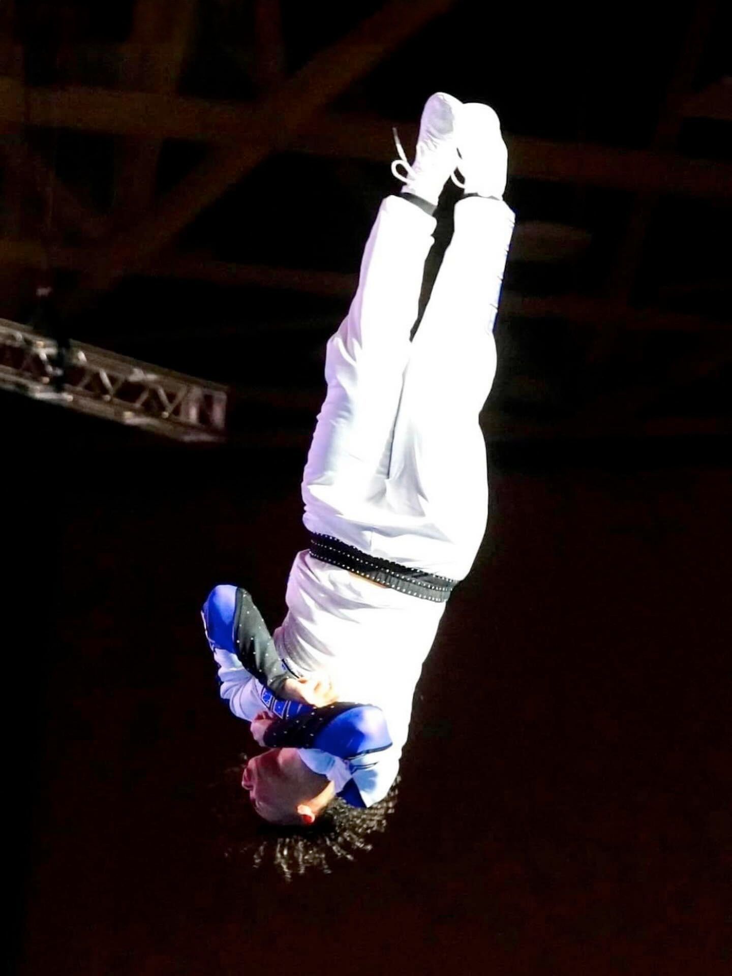 A person in white outfit upside down mid-air performing acrobatic move.