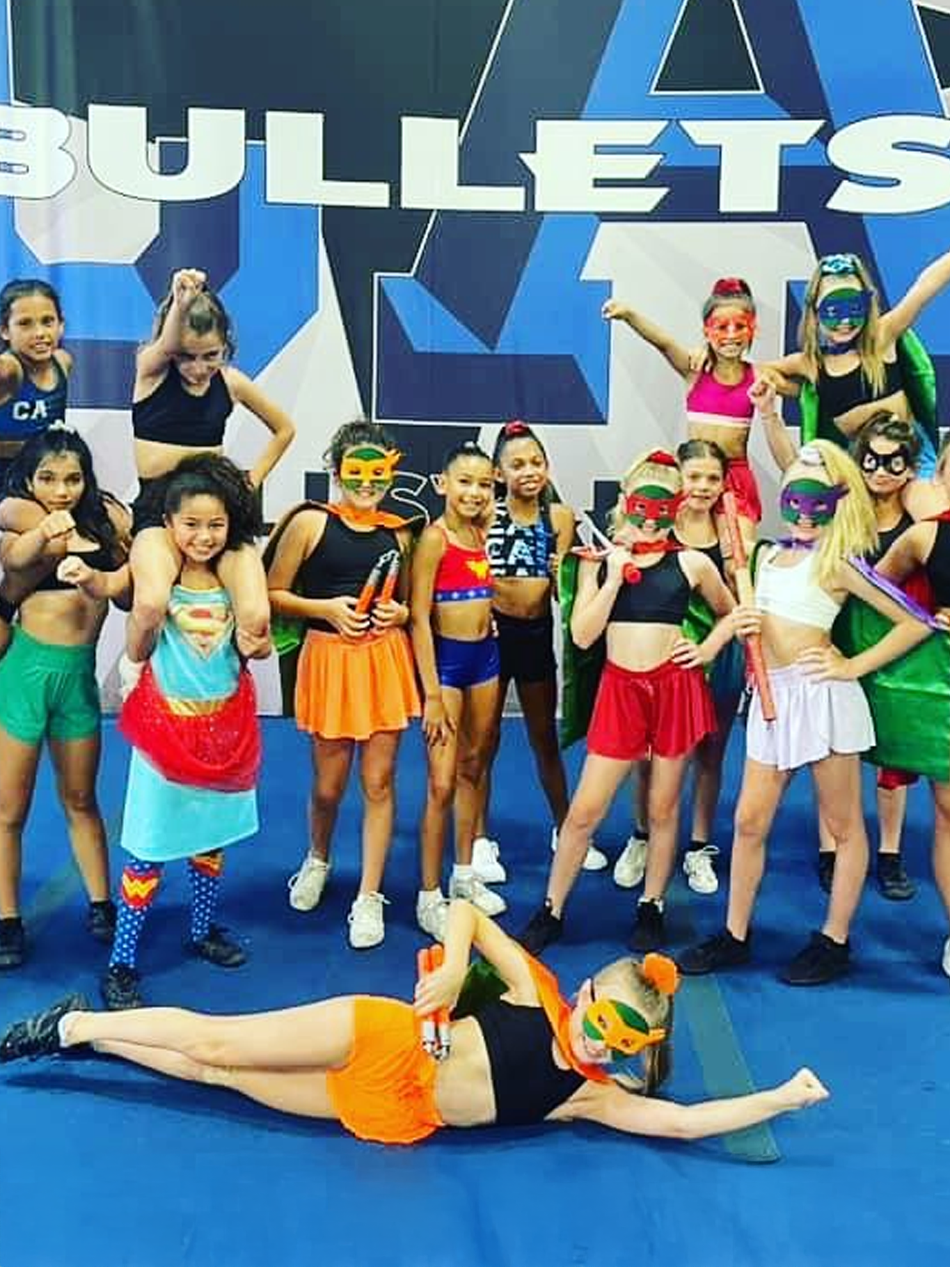 Cheerleaders in superhero costumes posing; blue gym, 