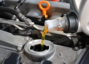 A close up of a person pouring oil into a car engine.