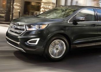 A black ford edge is driving down a city street.