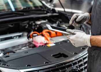 A mechanic is looking at a tablet while working on a car.