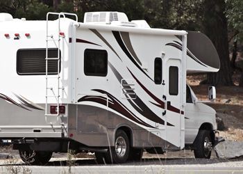 A white and brown rv is parked on the side of the road.