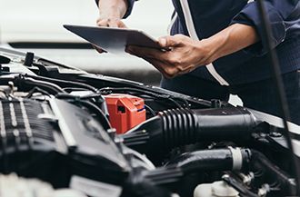 A mechanic is looking at a tablet while working on a car.