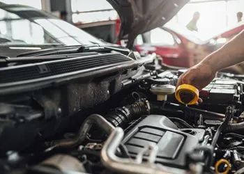 Mechanic checking car engine oil, hands holding a yellow oil cap, in a car repair shop.