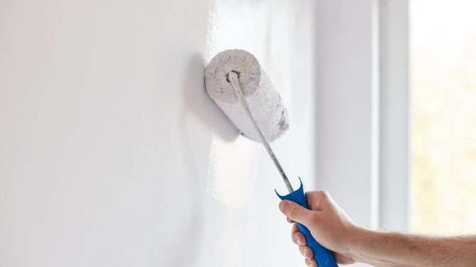 A person is painting a wall with a paint roller.