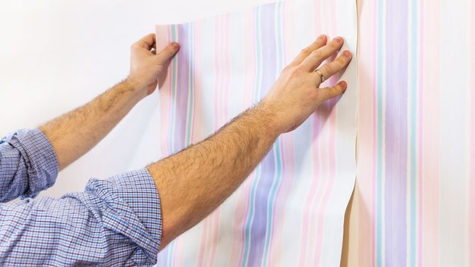 A man is installing a striped wallpaper on a wall.