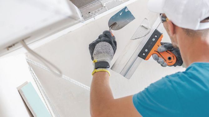 A man is plastering a ceiling with a spatula.