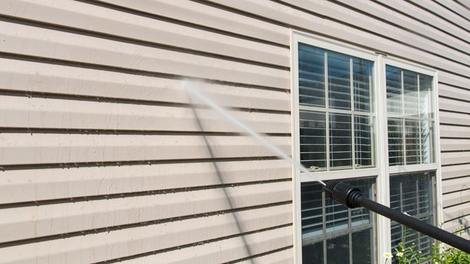 A person is cleaning the side of a house with a high pressure washer.