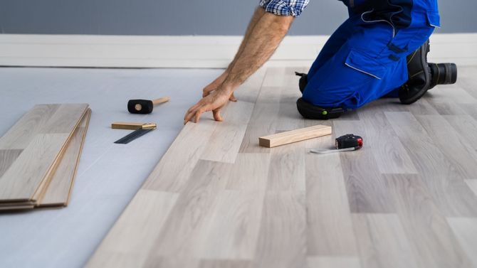 A man is kneeling down to install a wooden floor.