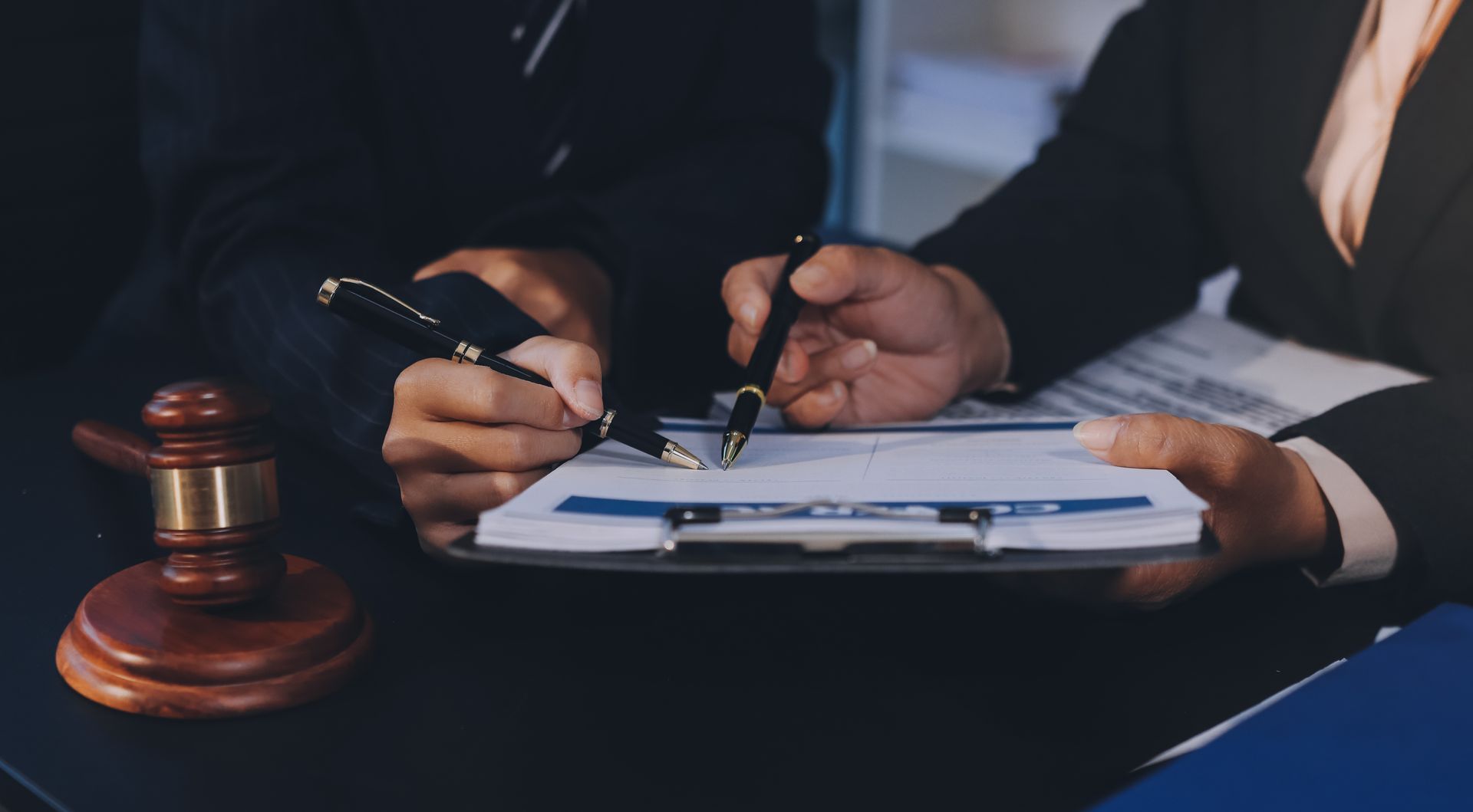 Two people reviewing documents, one holding a pen, gavel on the desk.