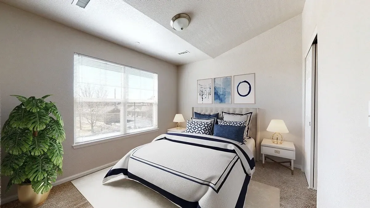 Bright bedroom with a neatly made bed, window light, a lamp, and a potted plant.