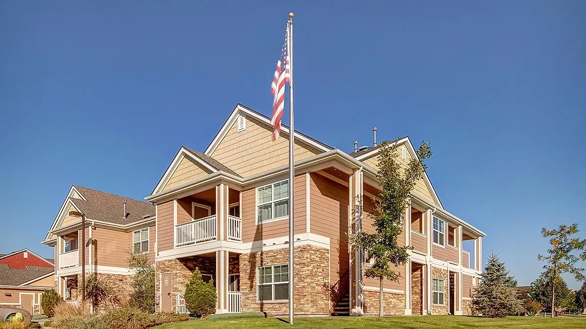 Two-story brick suburban house with a front porch and an American flag under a clear blue sky