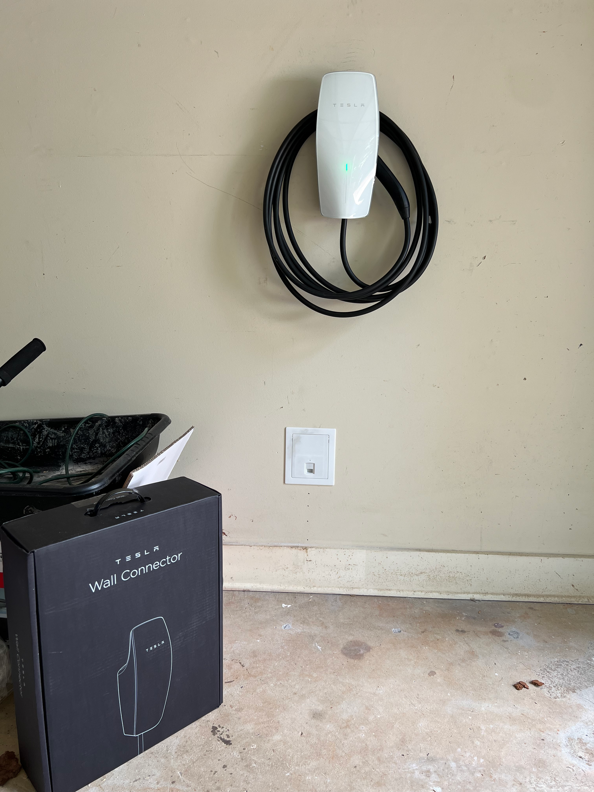 A tesla charging station is hanging on a wall next to a box.