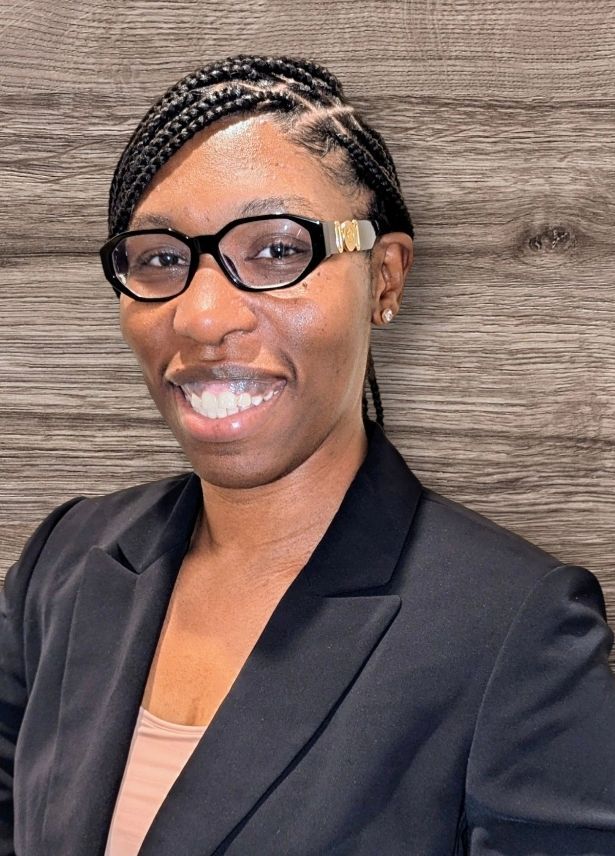 A woman wearing glasses and a black jacket is smiling for the camera.