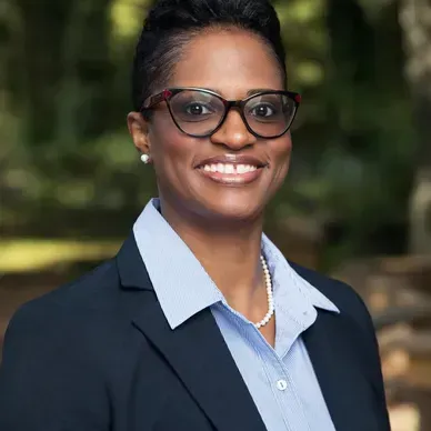 A woman wearing glasses and a suit is smiling for the camera.
