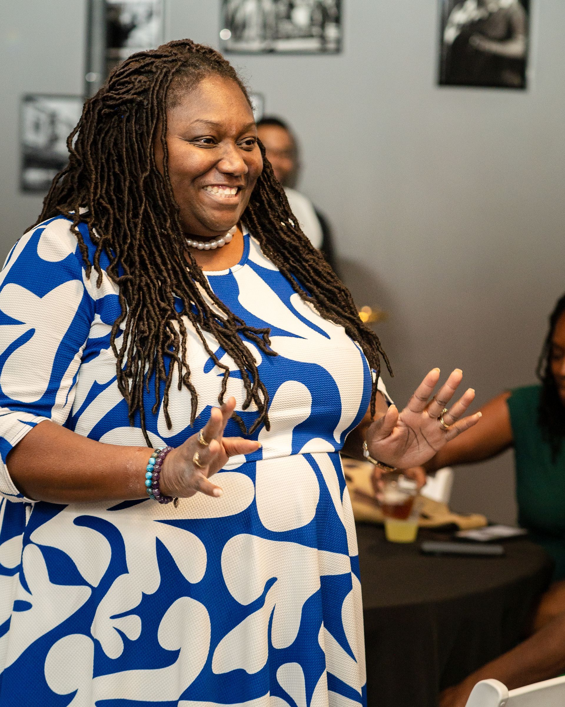 A woman in a blue and white dress is smiling and waving at the camera.