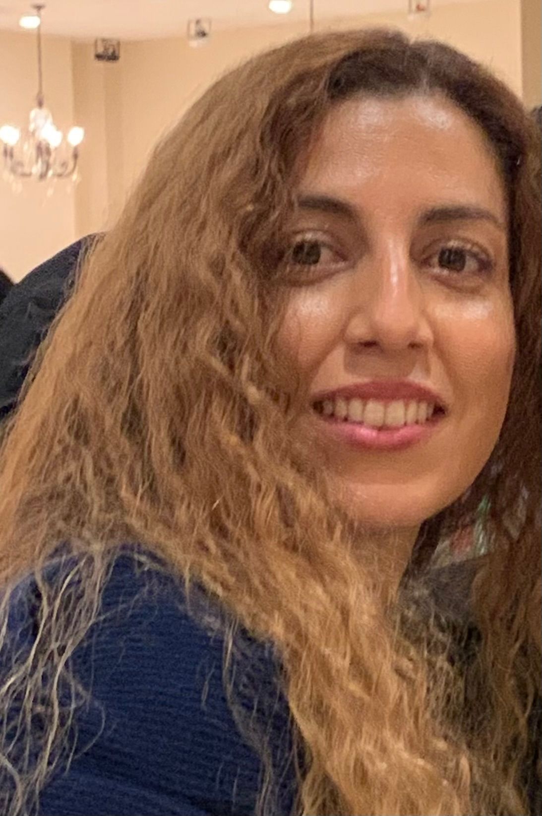 A woman with long blonde curly hair is smiling for the camera.