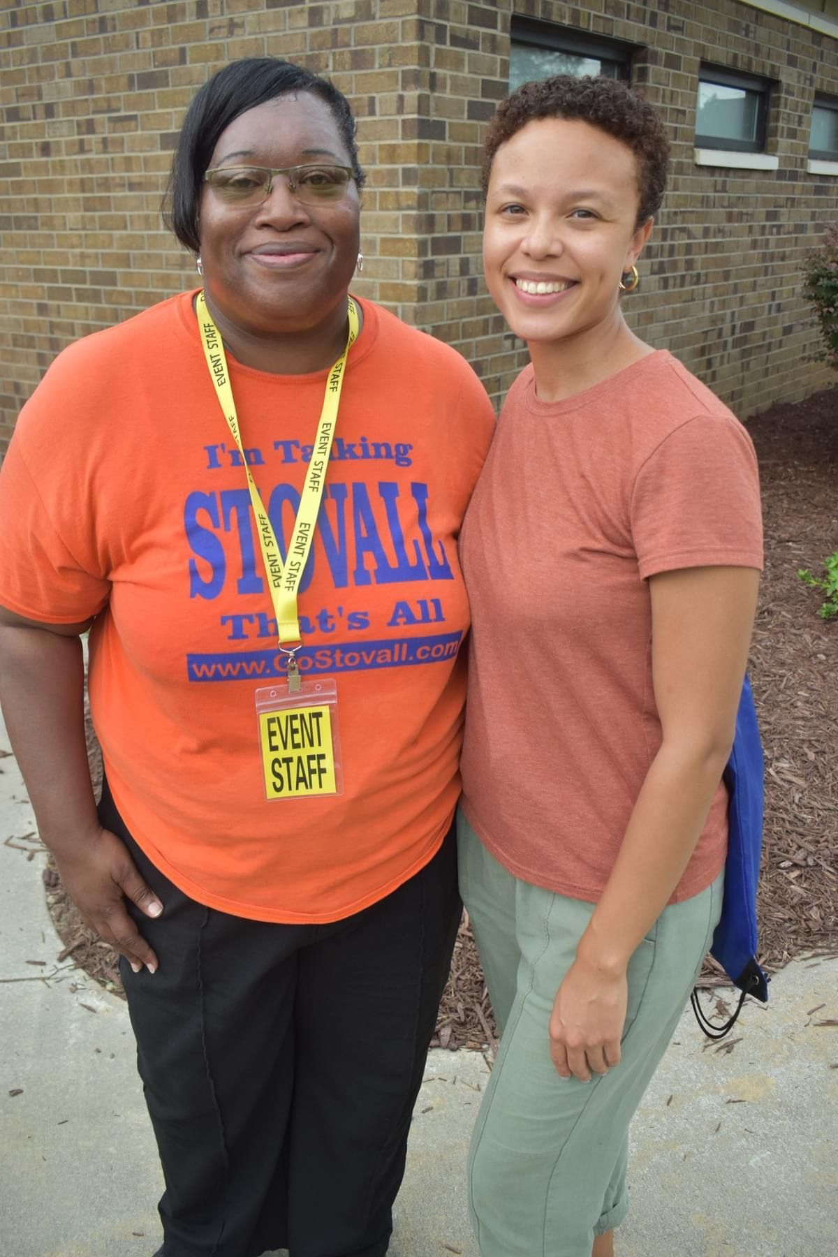 Two women posing for a picture one wearing an orange shirt that says i 'm talking st. wall