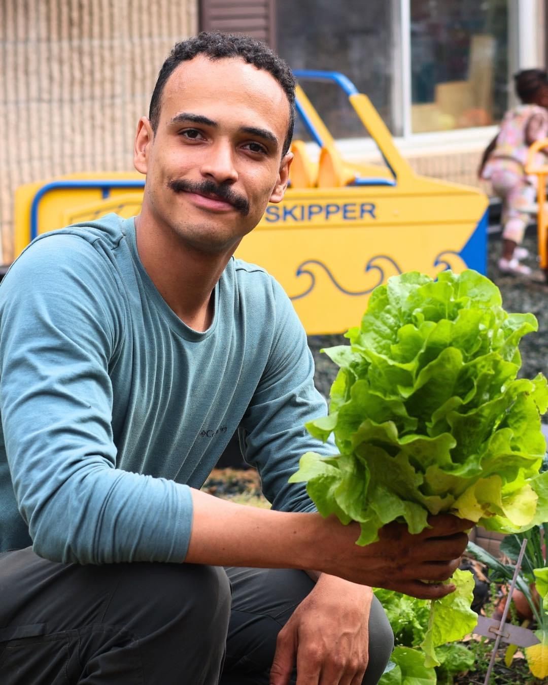 A man holding a bunch of lettuce in front of a yellow skipper
