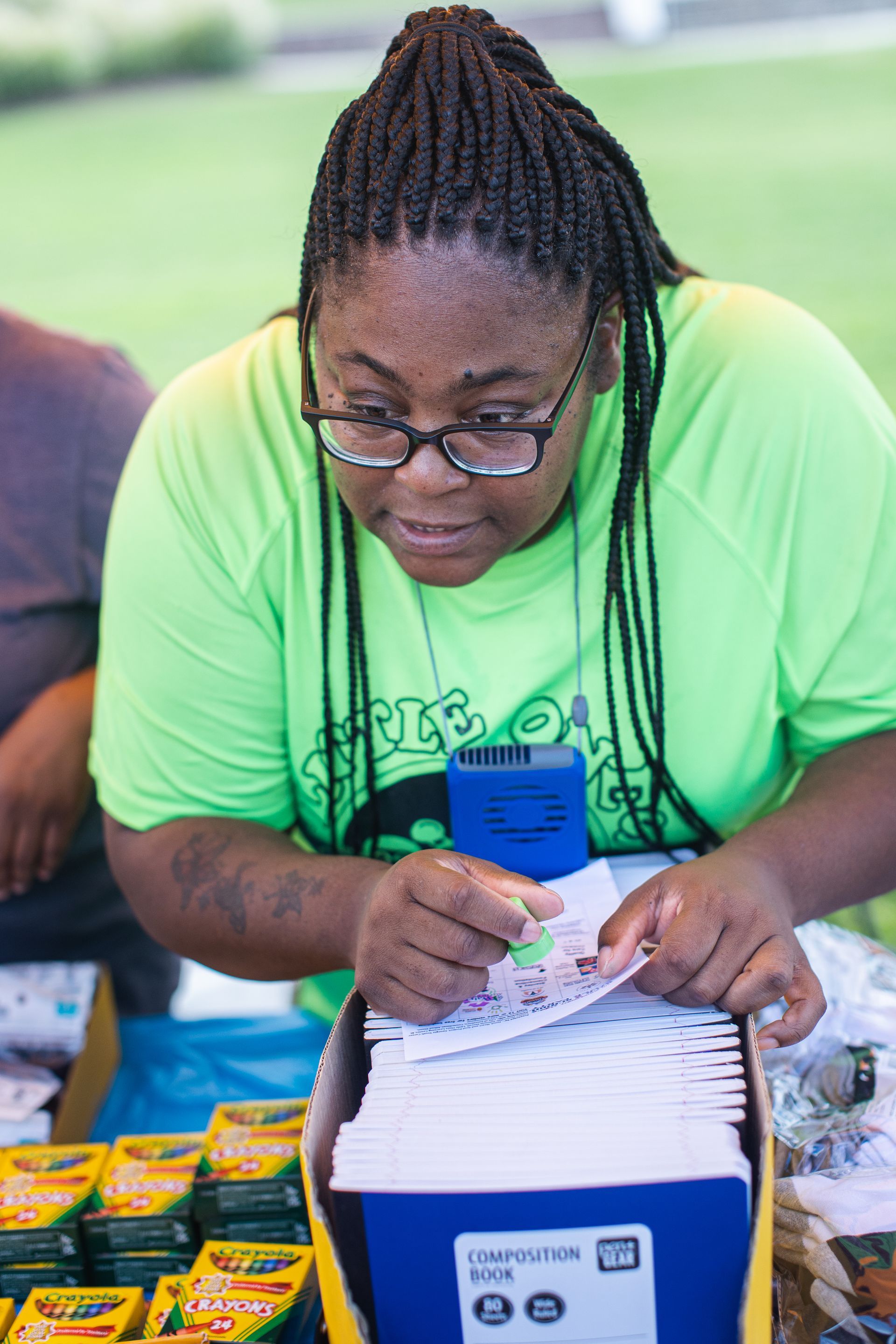 A woman in a green shirt is sitting at a table with a box of crayola crayons.