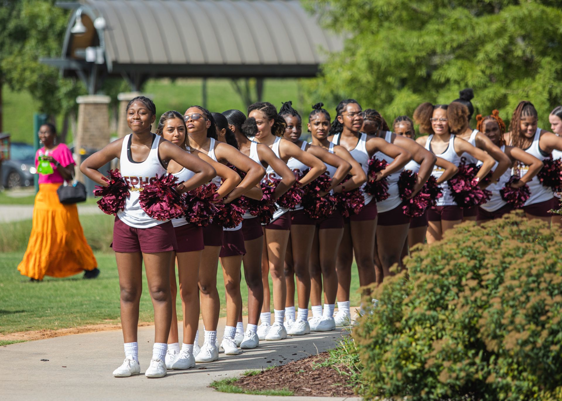 A group of cheerleaders are standing in a line on a sidewalk.