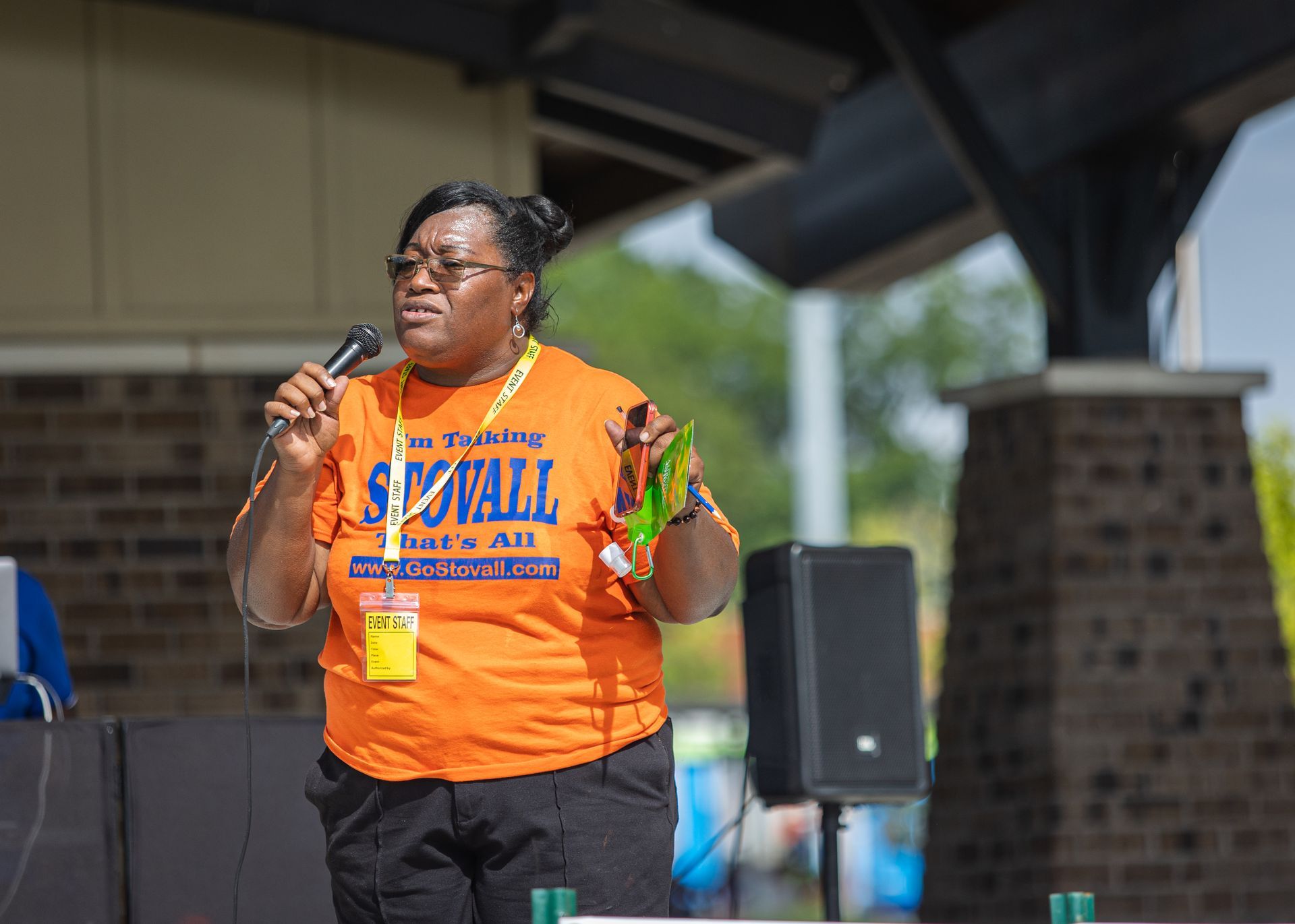 A woman in an orange shirt is speaking into a microphone.