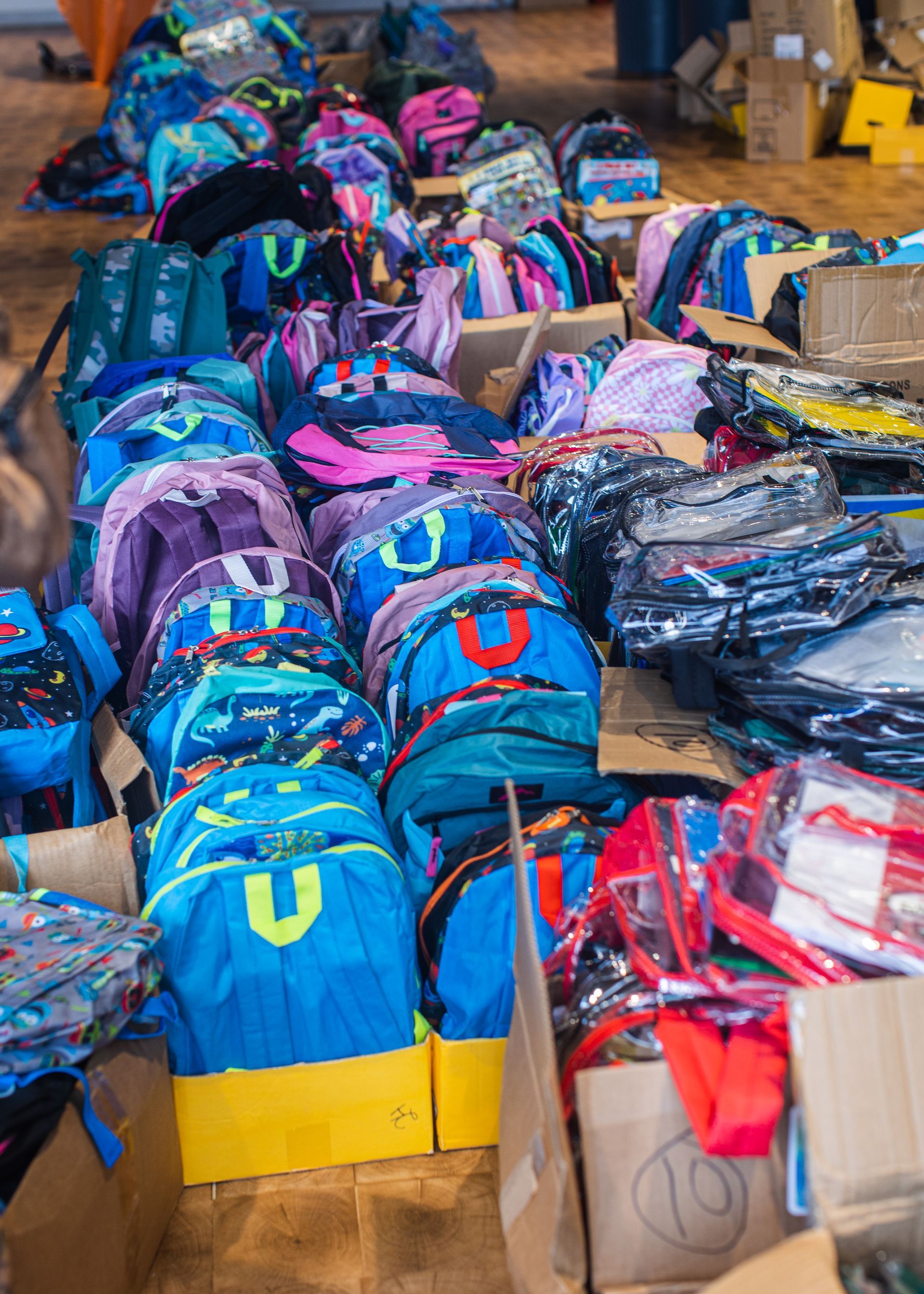 A bunch of backpacks are stacked on top of each other in boxes.