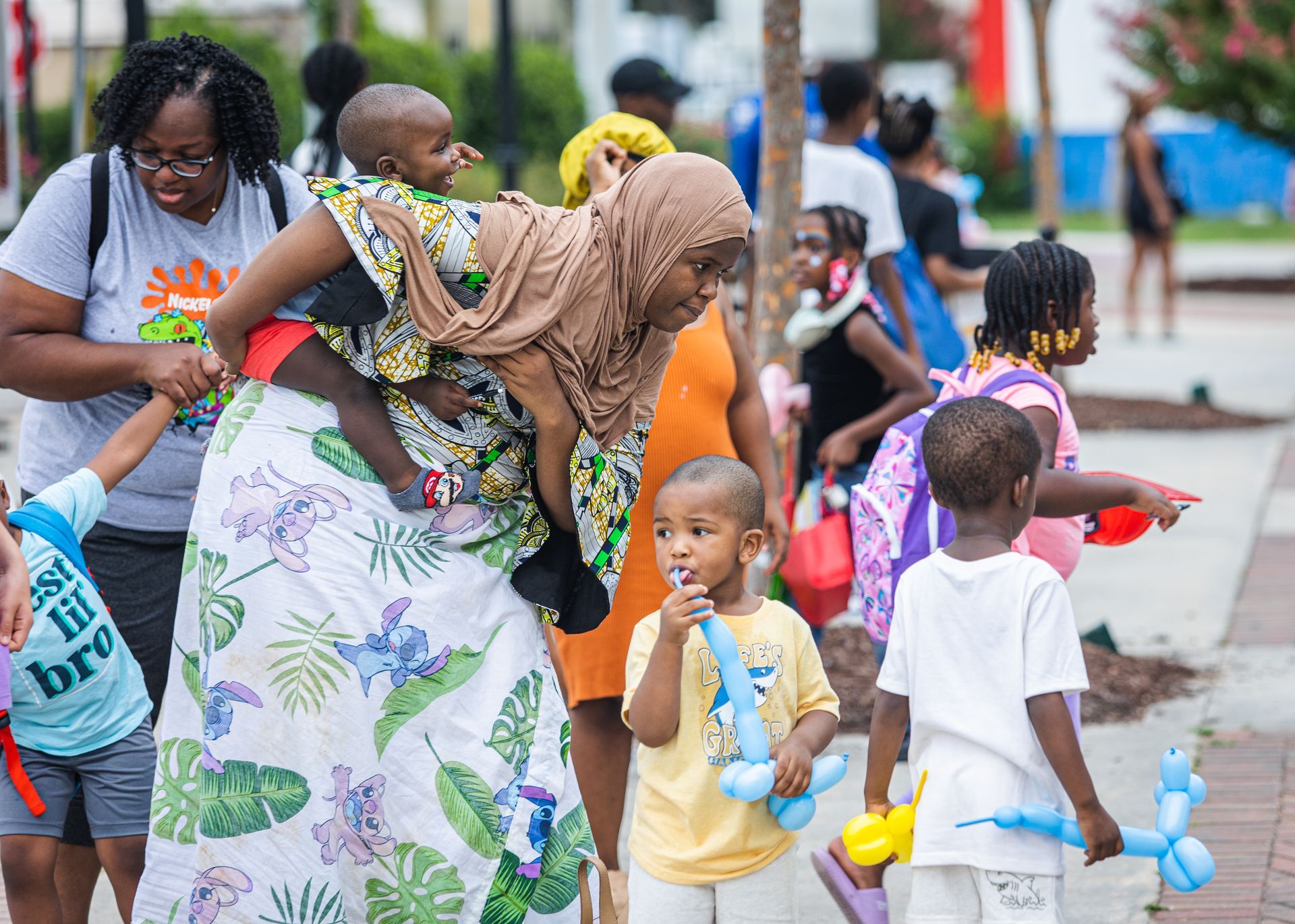 A woman is holding a baby in her arms while a group of children play with balloons.
